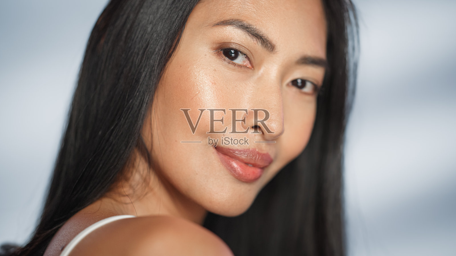 女性美丽的肖像。美丽的亚洲黑发女人摆姿势，微笑，触摸她的脸与自然，健康的皮肤。柔软孤立背景下的健康护肤理念。关闭了。照片摄影图片