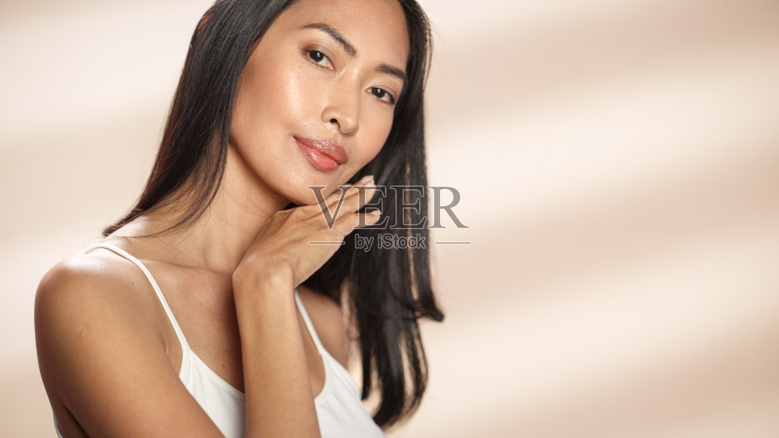 女性美丽的肖像。美丽的亚洲快乐的黑发女人摆姿势，触摸她的脸与自然，健康的皮肤。柔软孤立背景下的健康护肤理念。关闭了。照片摄影图片