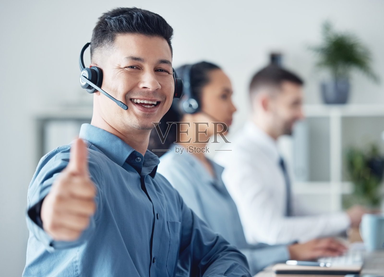 一个年轻的呼叫中心代理的肖像，在一个办公室里工作，与他的同事在背景中照片摄影图片