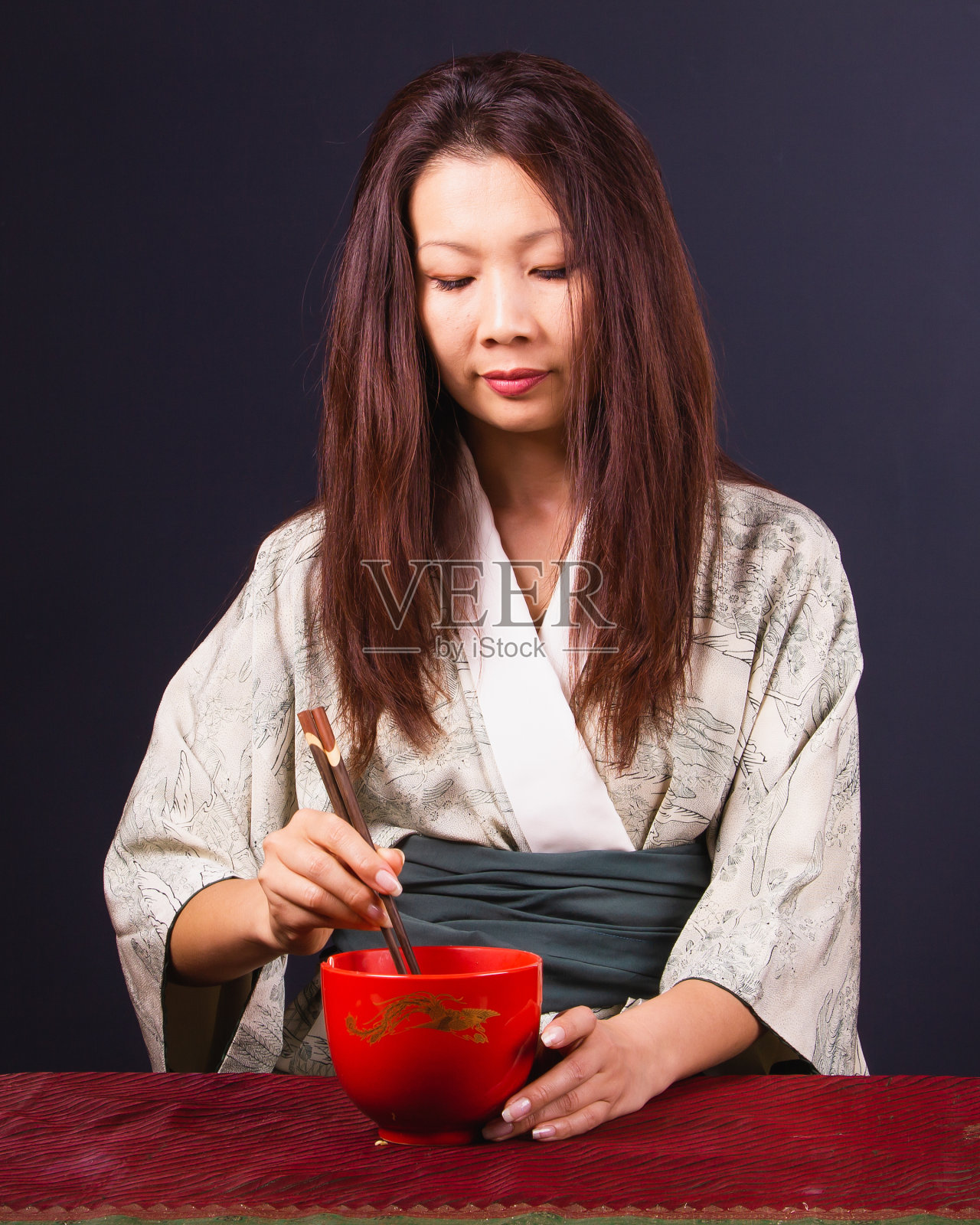 成年亚洲妇女在和服吃面与木筷子从一个红色的碗。照片摄影图片