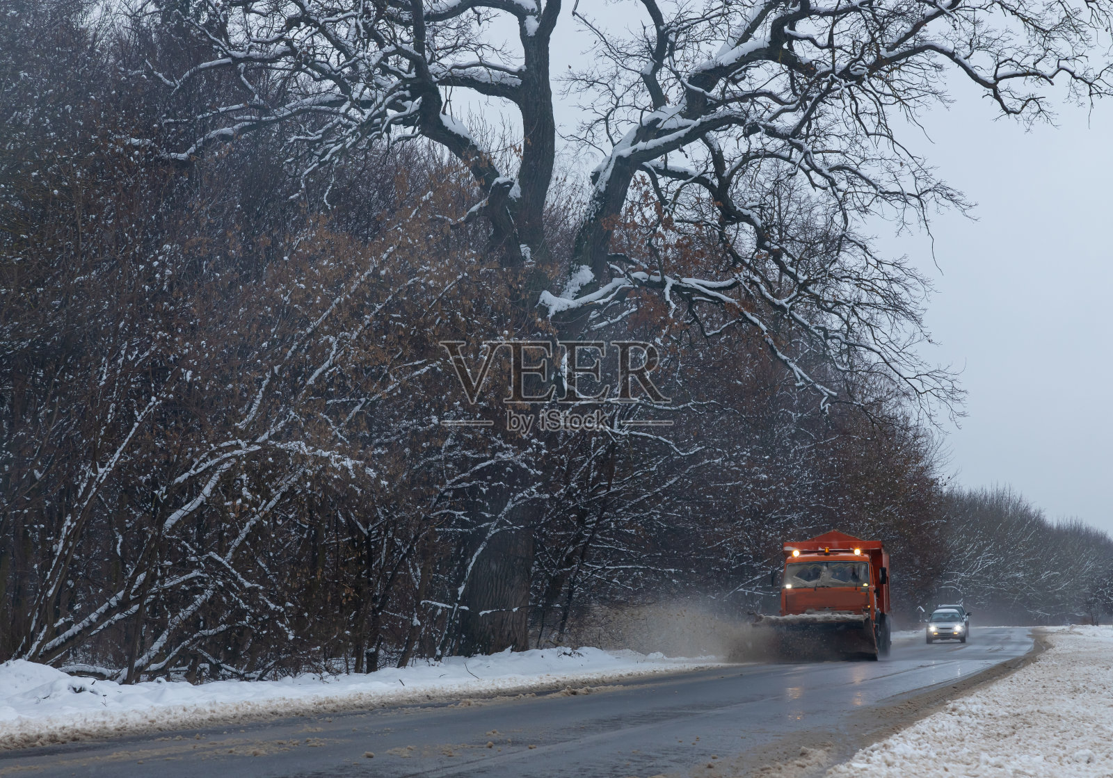 一辆载着犁的大车清除路上的积雪。橙色货运的特殊设备正在与冬天的恶劣天气作斗争。消除暴风雪的影响。交通困难。冷冻水照片摄影图片