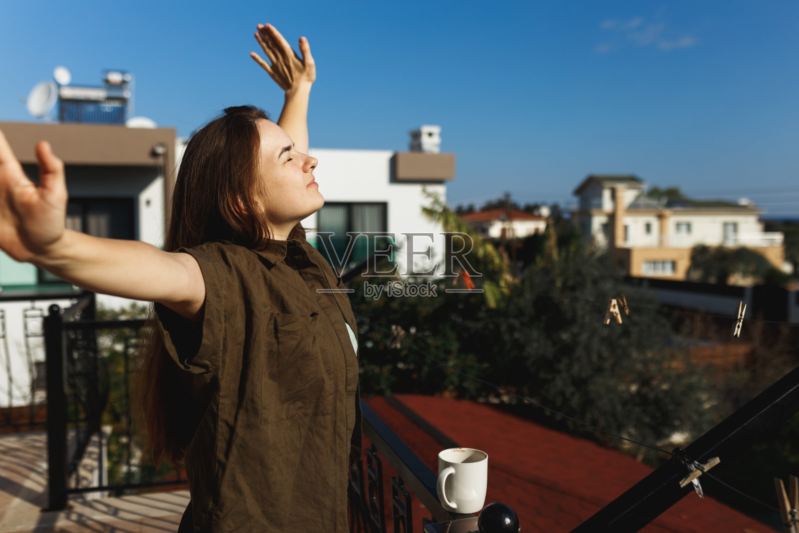 一个幸福的女人张开双手在阳台上喝咖啡的肖像。放松，思考，转移视线。在户外的阳光下，享受她的早茶。室内自然柔和照片摄影图片