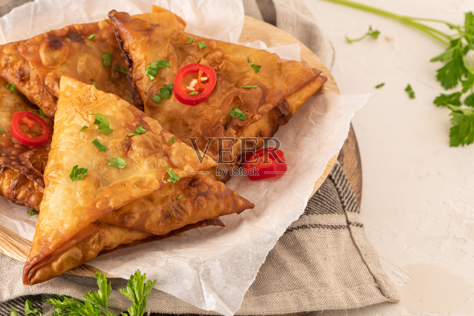 印度三角饺——油炸或烘烤的糕点与可口的馅料，流行的印度小吃，服务与酸奶酱在槟榔叶菜与香料在厨房的工作台面。照片摄影图片