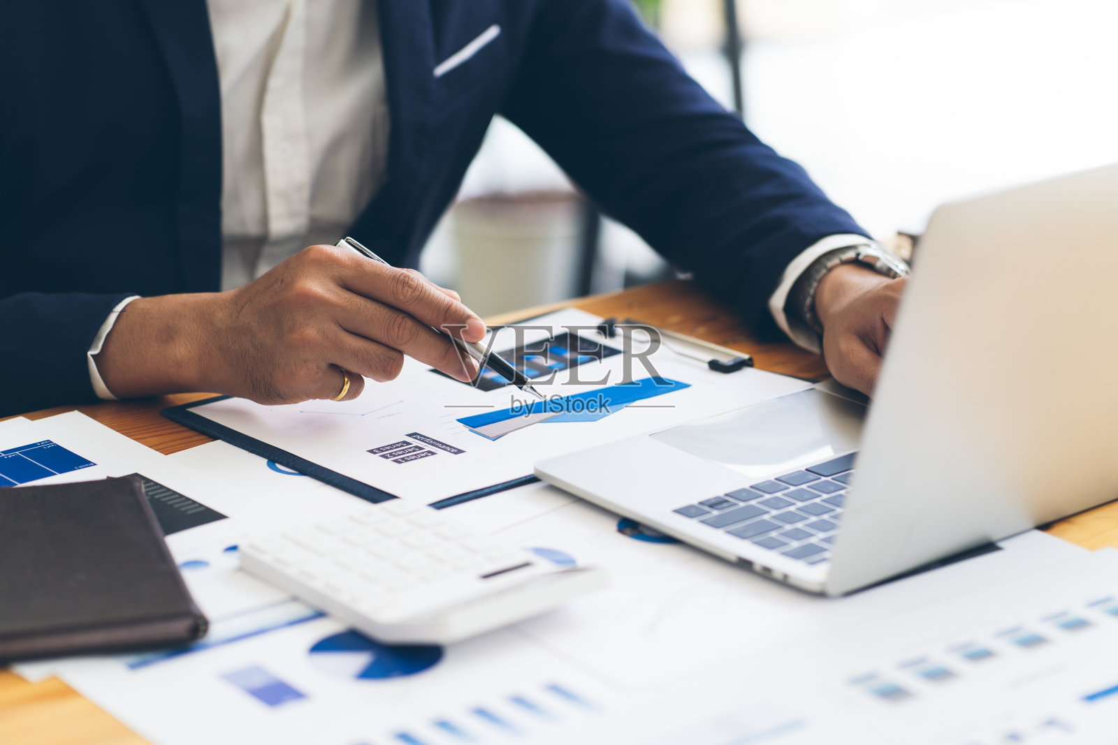 商务人员拿着笔，指着纸，用笔记本电脑分析年度业务报告。照片摄影图片