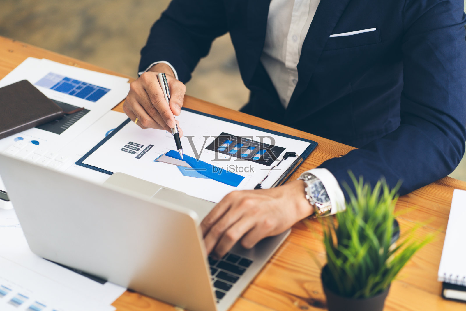 商务人员拿着笔，指着纸，用笔记本电脑分析年度业务报告。照片摄影图片