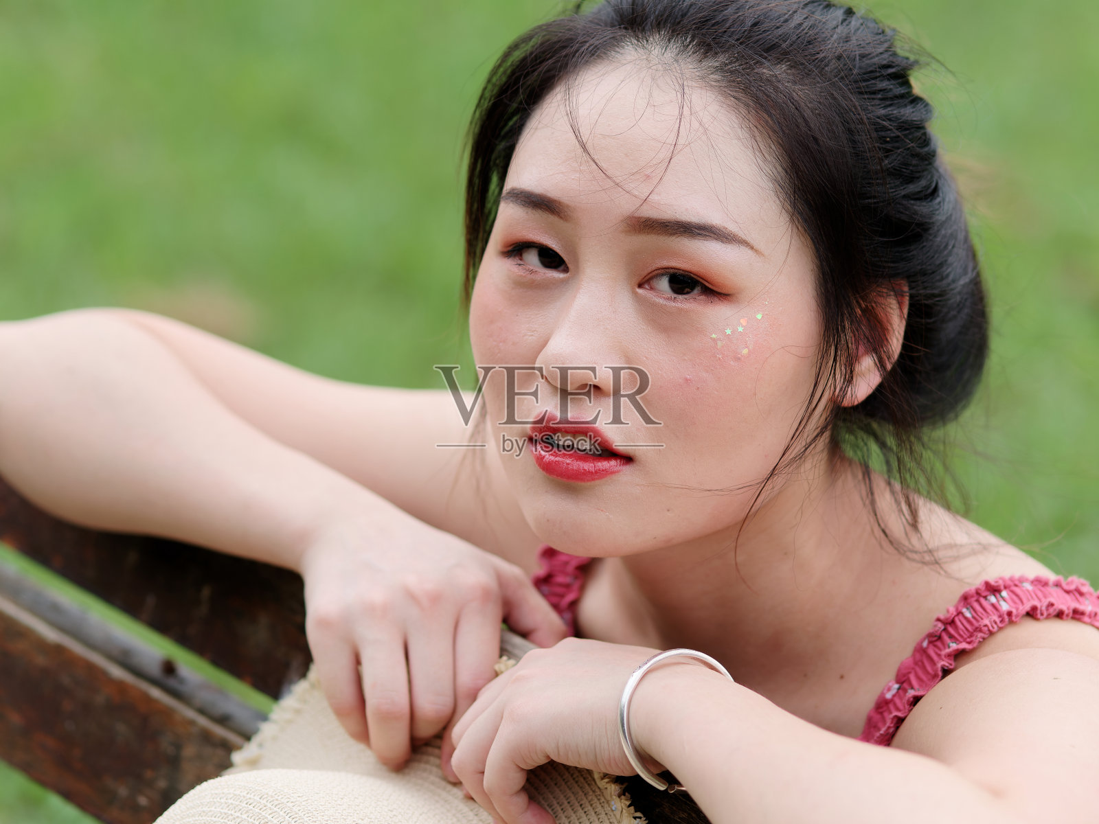 年轻的亚洲女人的肖像看着和微笑的头在她的手与自然的背景，美丽的中国女孩在性感的红色连衣裙享受她的无忧无虑的时间在炎热的夏天，近距离的镜头。照片摄影图片