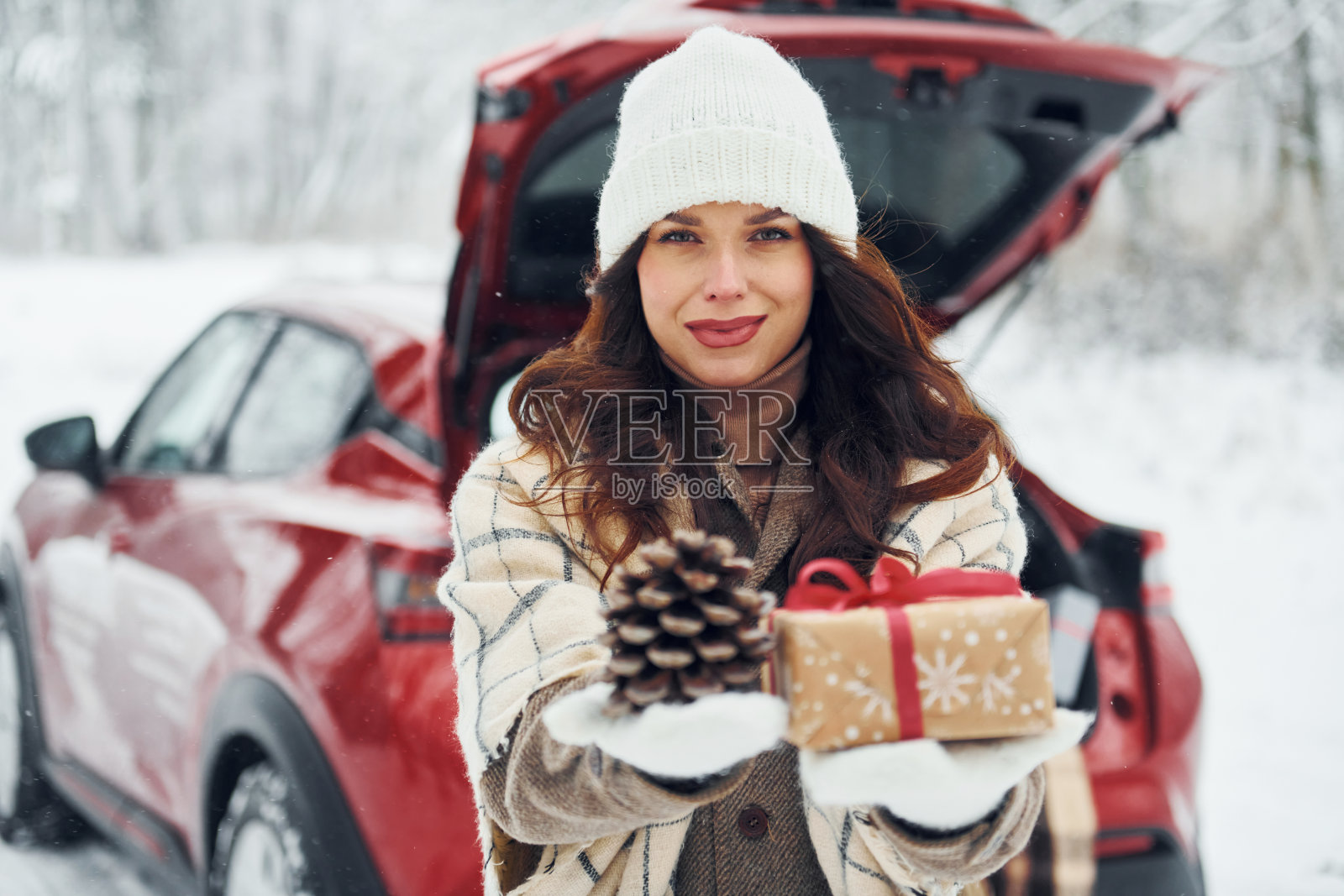 拿着礼物盒。冬天的时候，美丽的年轻女子在户外，靠近她的红色汽车照片摄影图片