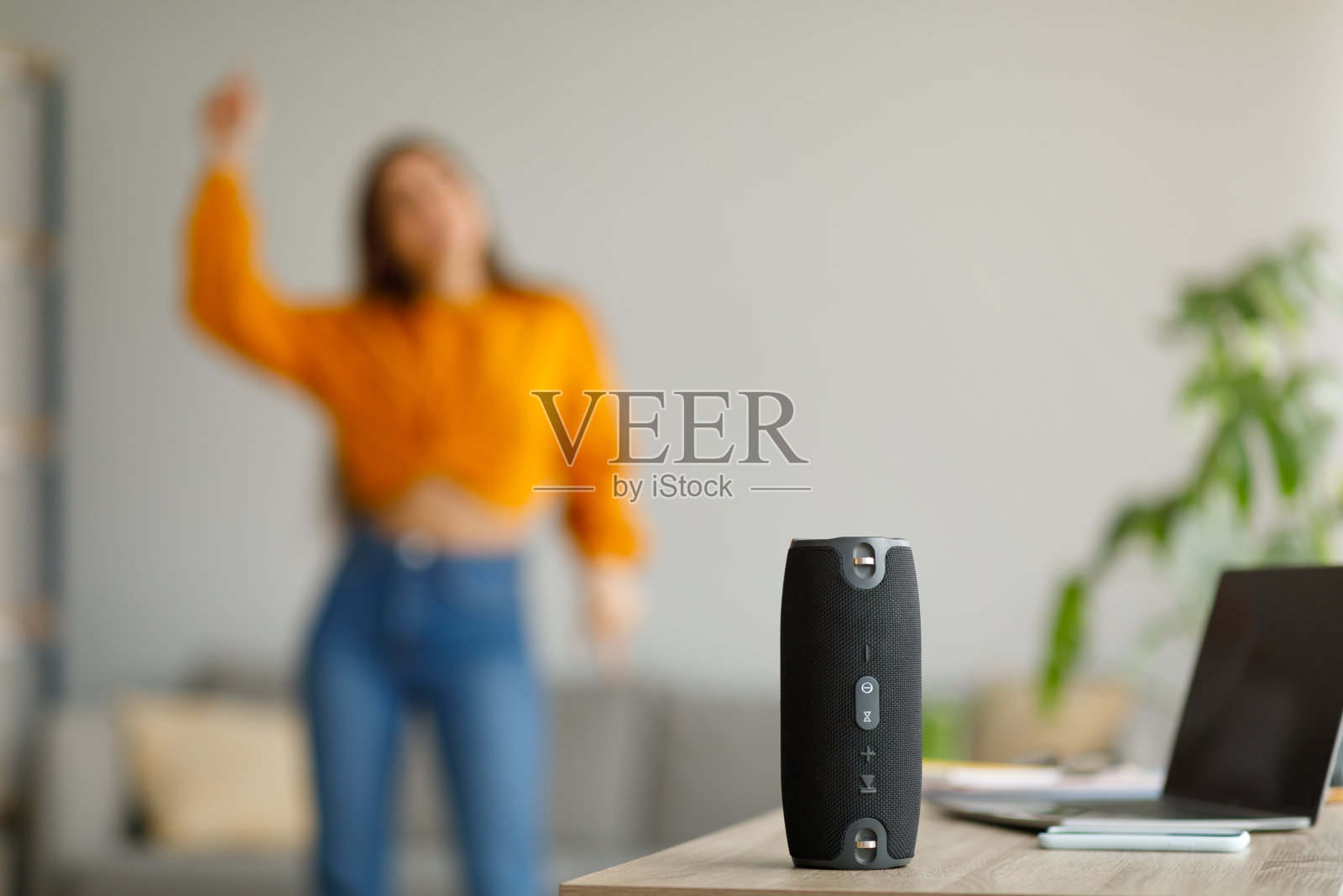 年轻的女士在家里随着流行音乐跳舞，选择性的集中在便携式无线扬声器，拷贝空间照片摄影图片