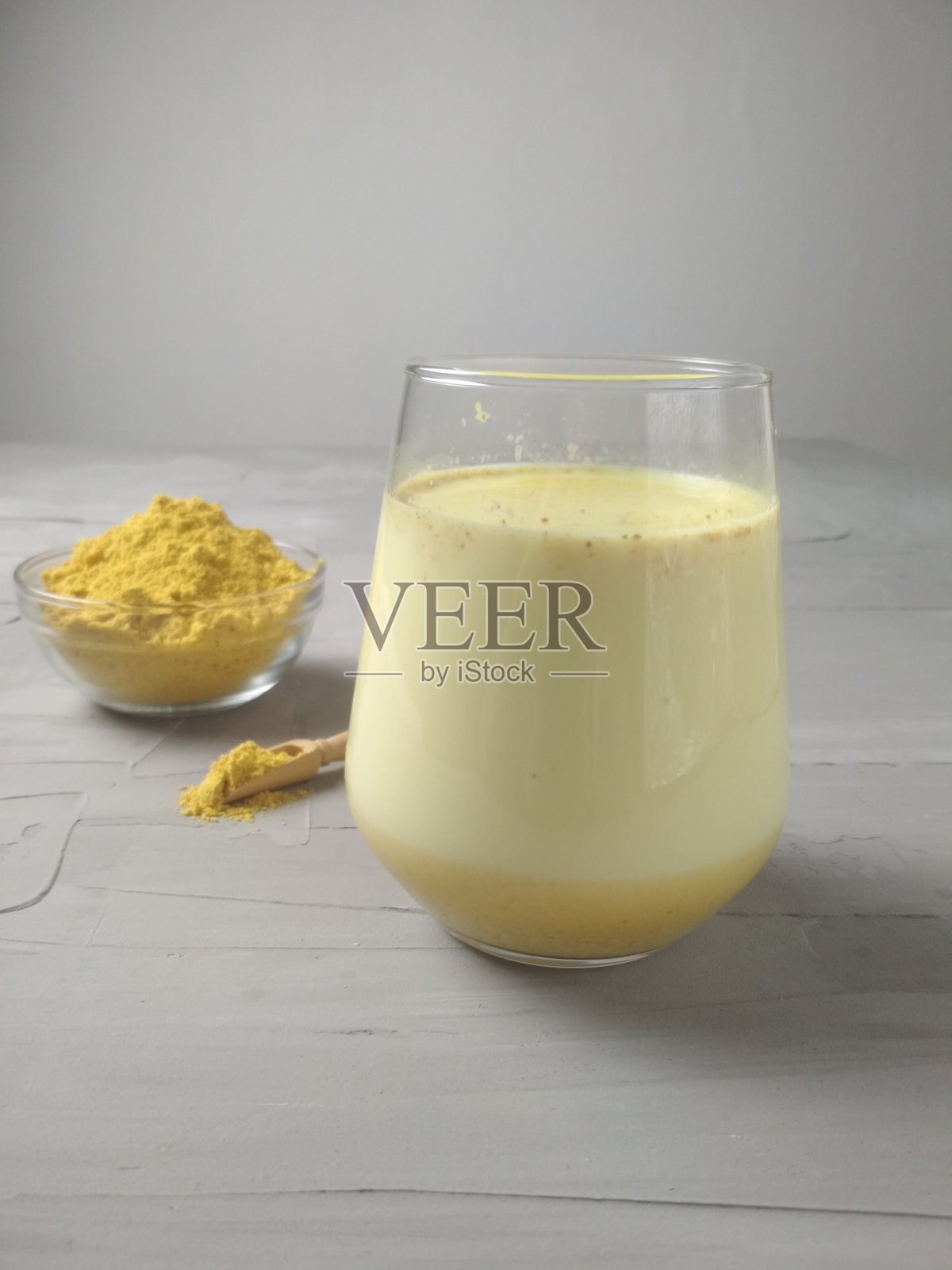 金色的牛奶放在灰色的玻璃上，旁边放着姜黄调味料。健康的饮料。添加了姜黄的黄色牛奶。治疗照片摄影图片