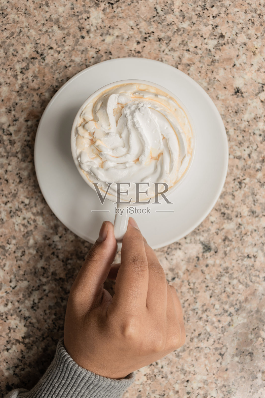 一杯美味的奶油咖啡，在有质感的桌子上握着杯子的手的细节，工作室里的生活方式和饮料照片摄影图片