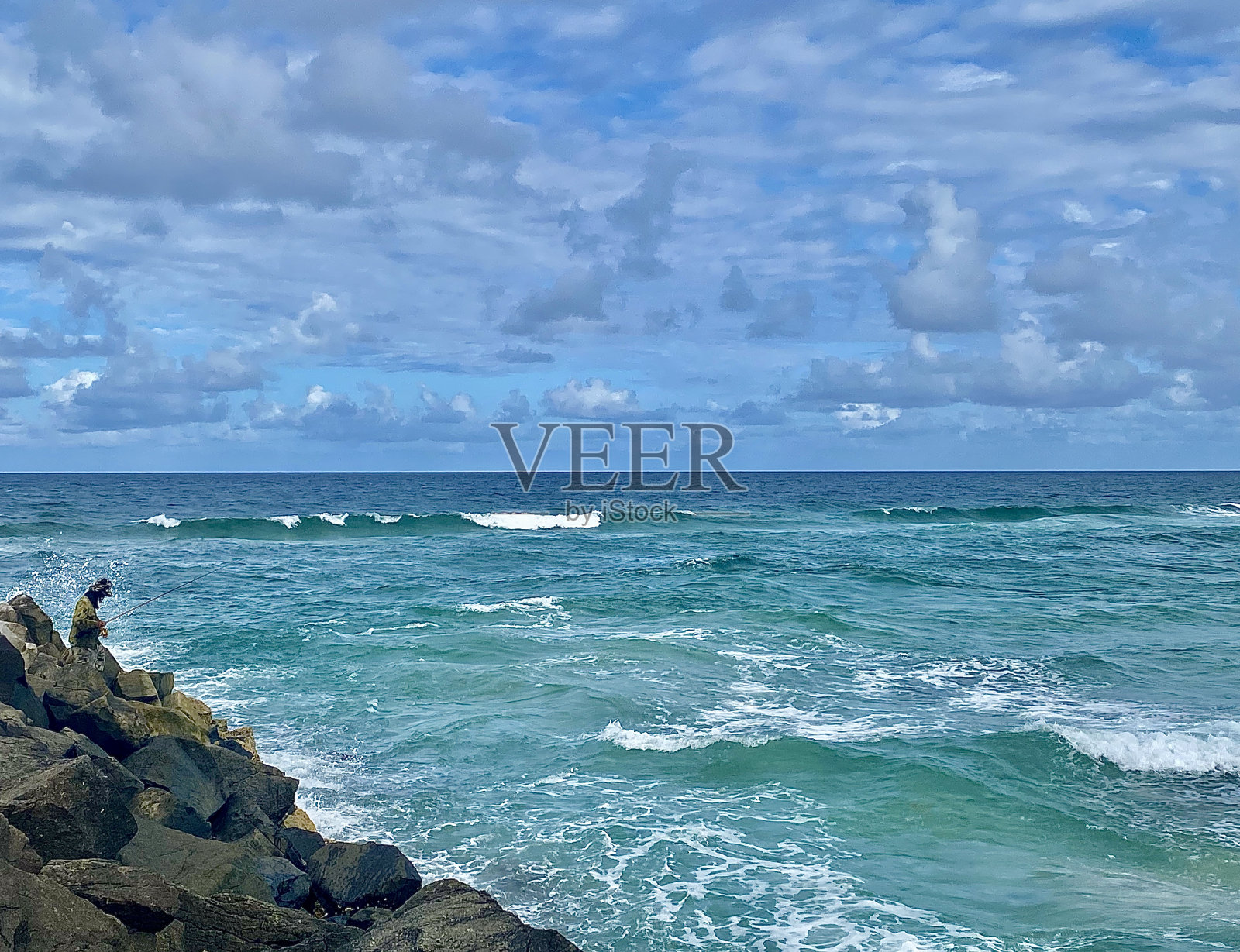 在暴风雨的海洋中，在海滨岩石上钓鱼照片摄影图片