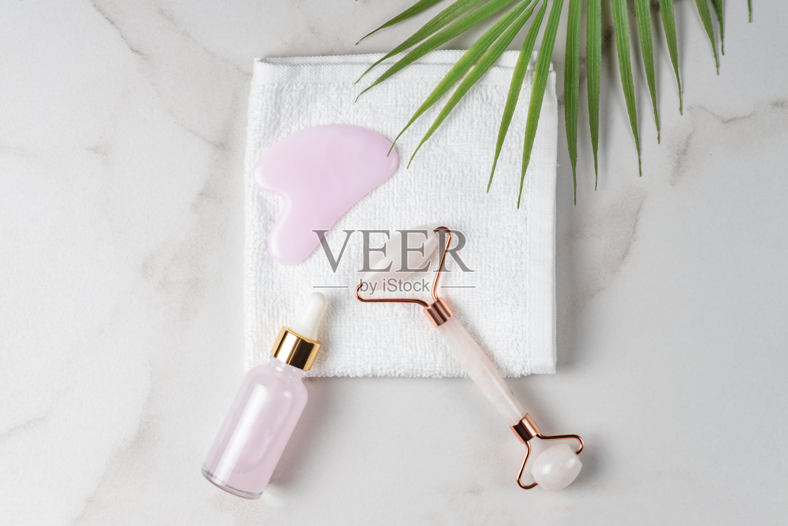 皮肤护理的概念。装有洁面精华或洁面油的瓶子。石英滚筒和刮痧按摩刮刀。在大理石背景上的白色棉纺毛巾上的化妆品和工具照片摄影图片