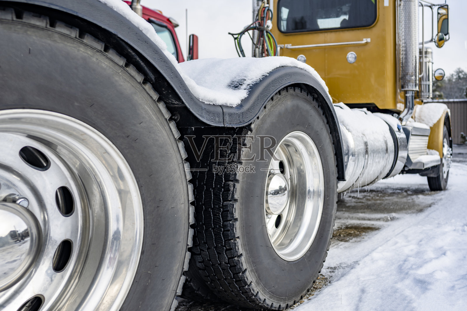 黄色专业日间驾驶室大型钻机半挂车双轴车轮和轮胎与一个大胎面站在冬季停车场的冰雪照片摄影图片