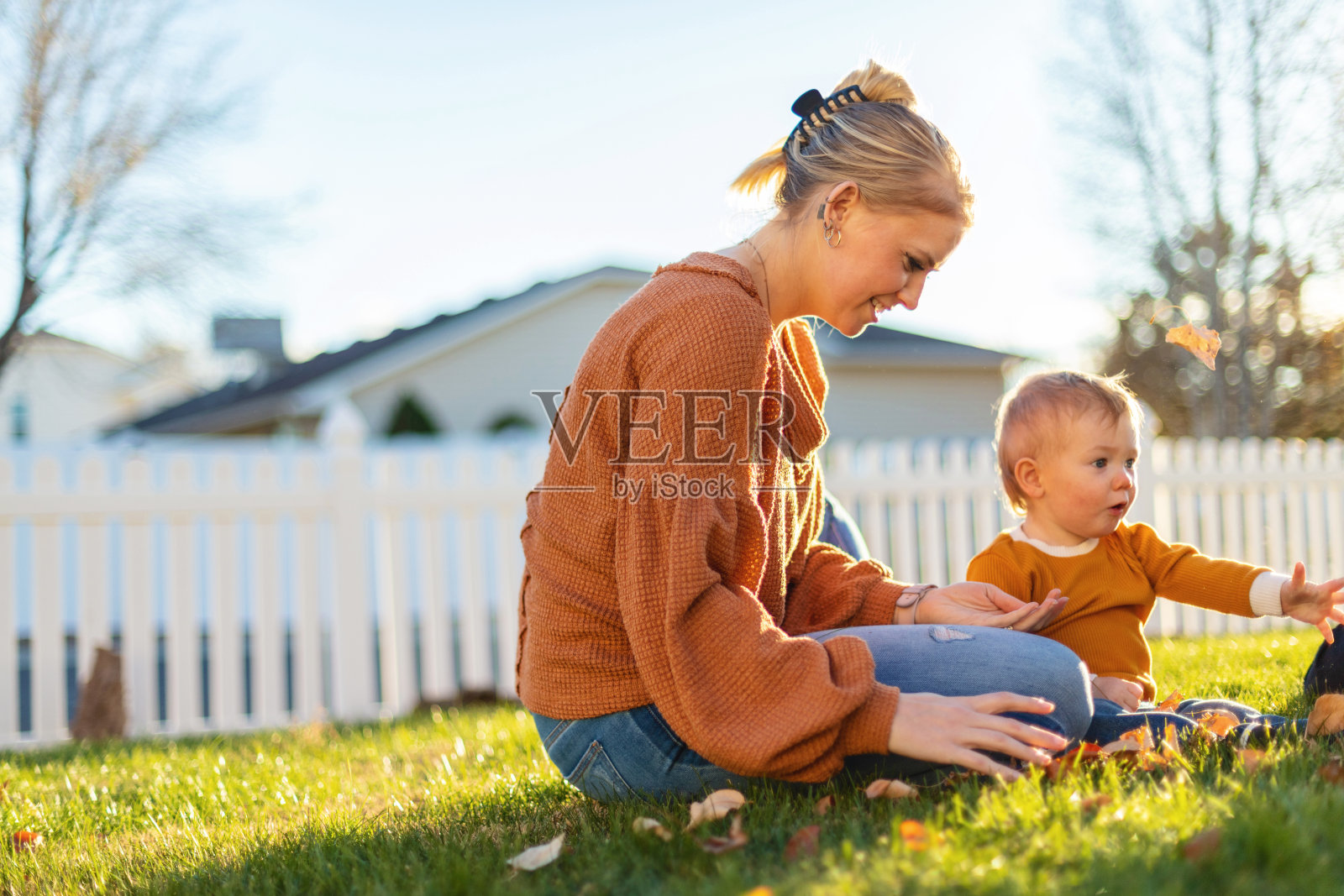 在树叶中玩耍，夏末初秋，母亲和男孩与祖母一起在院子里玩耍照片摄影图片