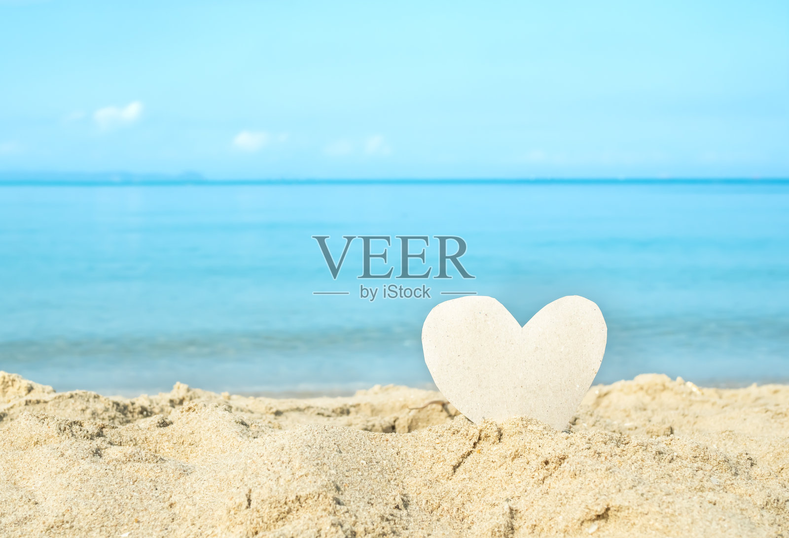 心形模型纸在沙滩上与模糊的蓝色的海和蓝色的天空背景。照片摄影图片