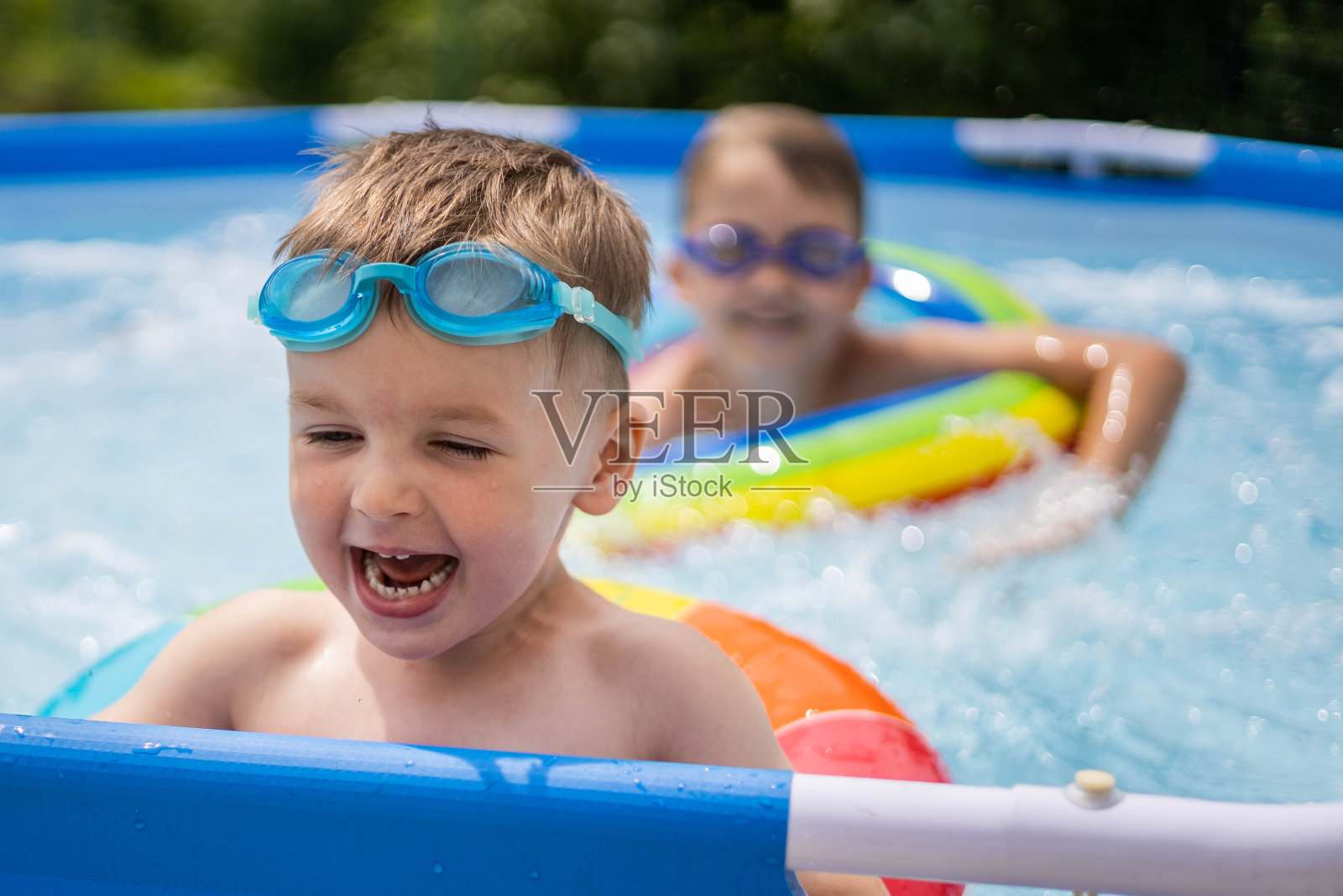 两个男孩兄弟在屋外屋外的游泳池里游泳和玩耍。彩色的，游泳的，明亮的，彩虹的圆圈照片摄影图片