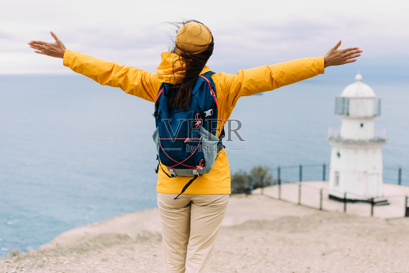 一个背着背包的女人站在大海的背景下举起双手，后视镜。旅游、旅游和积极的生活方式理念。这个女孩去美丽的地方旅行。照片摄影图片