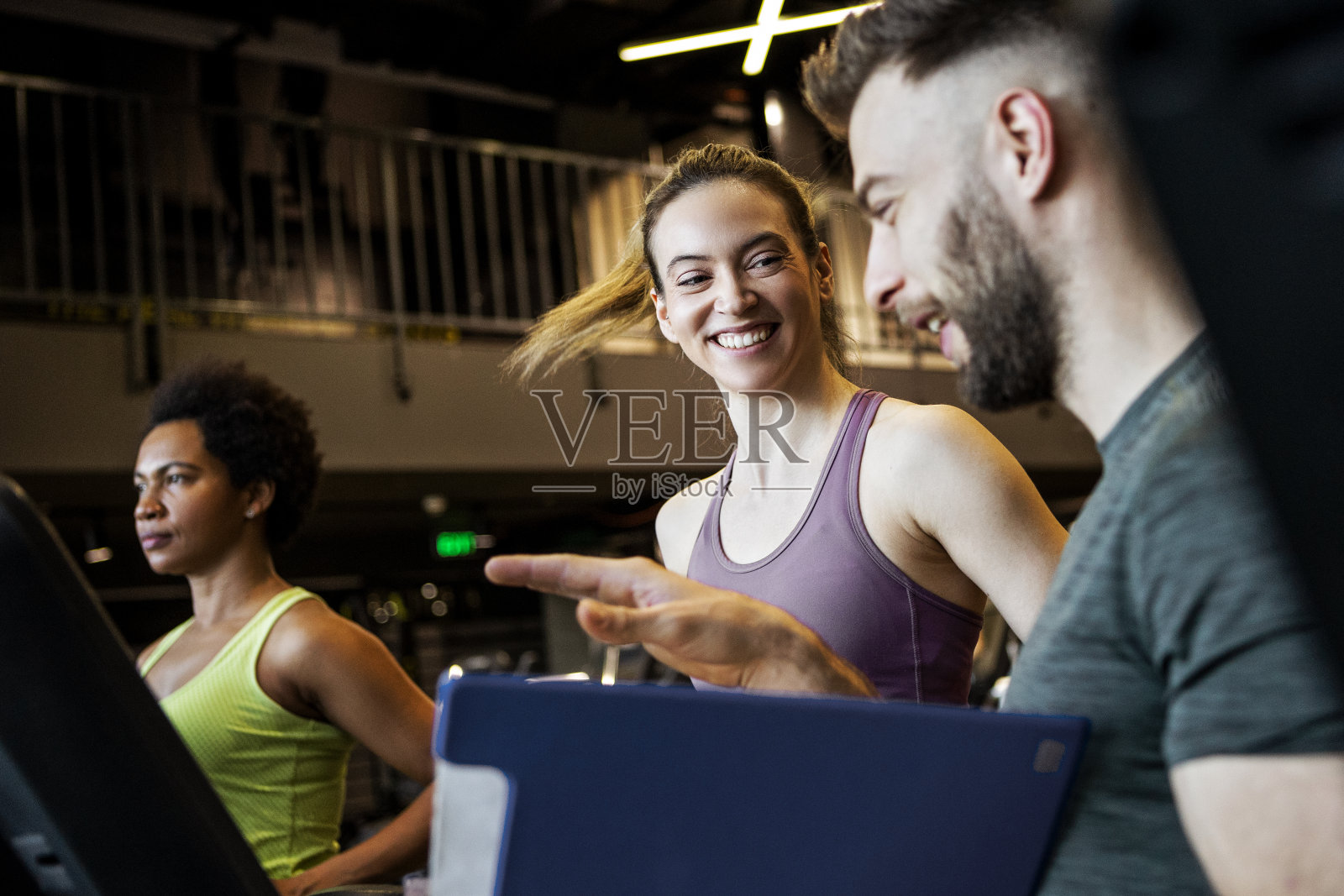 微笑的年轻女子和私人教练在健身房的跑步机上照片摄影图片