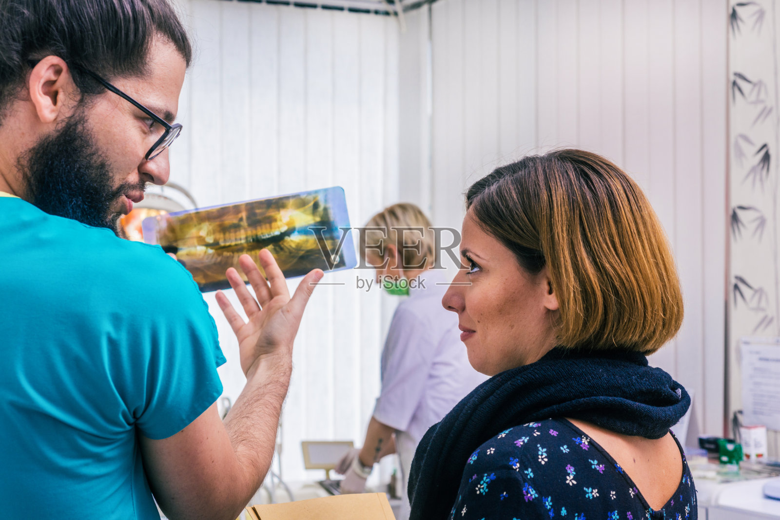 留着胡子的牙医戴着眼镜看着牙科x光扫描，和他的女病人交谈。照片摄影图片