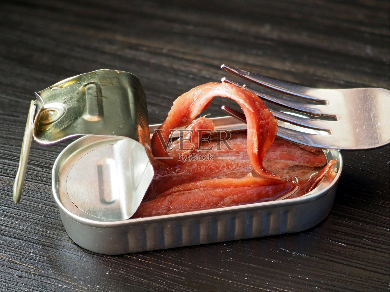 盐腌凤尾鱼片在叉的背景下，一个开放的罐头与鱼照片摄影图片