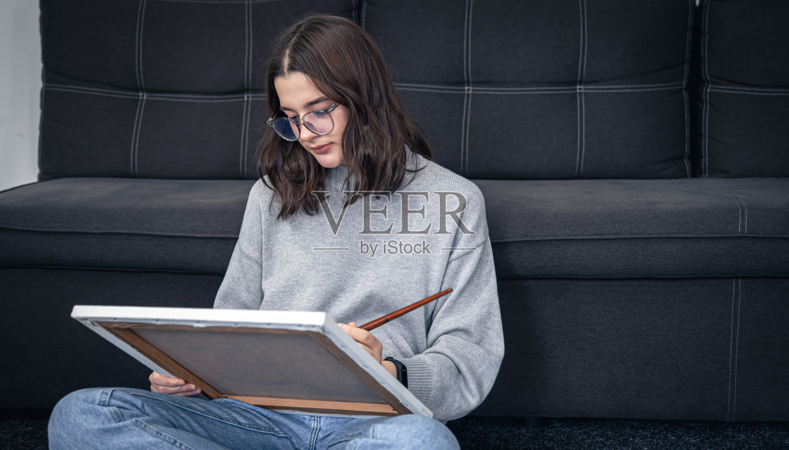 一位年轻女子正坐着在画布上画画。照片摄影图片