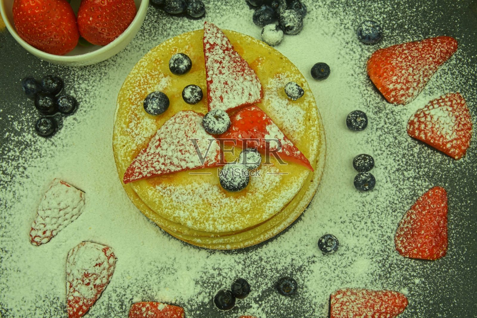 黑色背景上的水果浆果煎饼。新鲜的薄煎饼。蓝莓，草莓和煎饼上的糖粉。平躺照片摄影图片