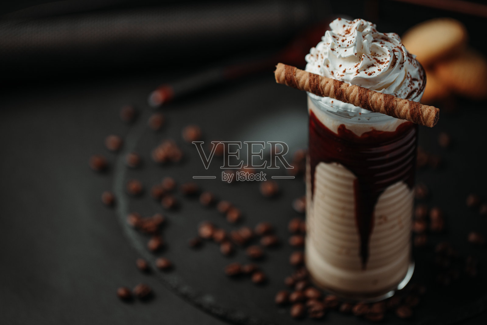 一杯热巧克力或咖啡的特写镜头，上面有鲜奶油，巧克力屑和甜点，散落在黑色背景的黑色盘子里的咖啡豆照片摄影图片