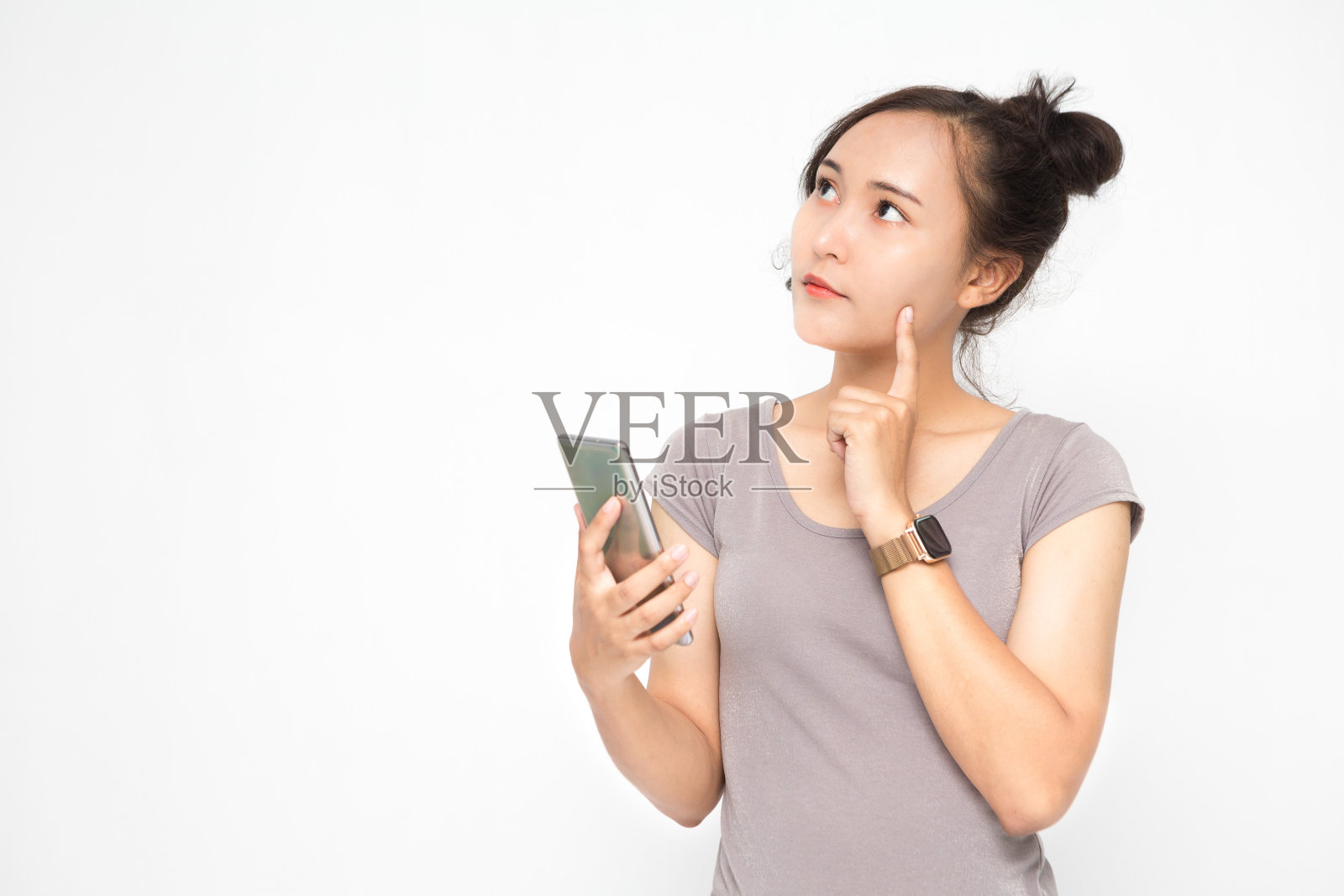 美丽的亚洲妇女穿着灰色休闲衬衫拿着智能手机在白色背景和复制空间。可爱的亚洲女人正在思考和聊天关于社交媒体的概念照片摄影图片