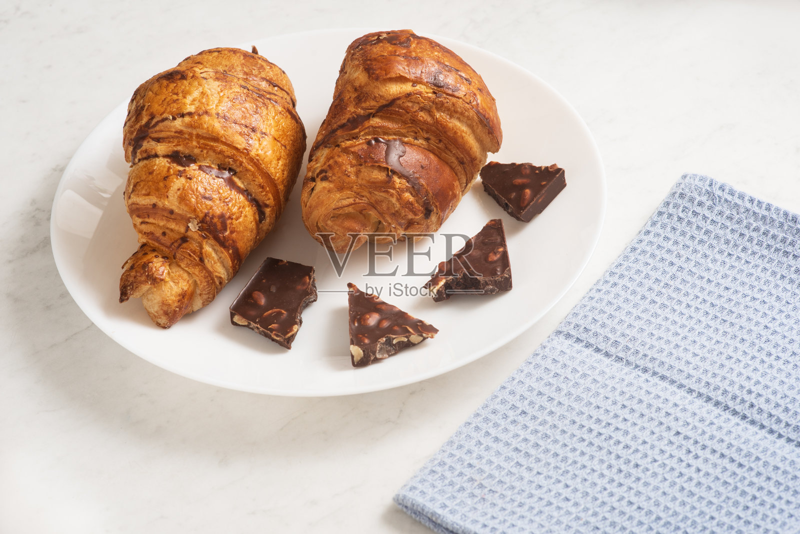 美味、开胃、酥脆的羊角面包，配上黑巧克力和厨房毛巾，放在大理石桌子上的盘子里。法国糕点照片摄影图片
