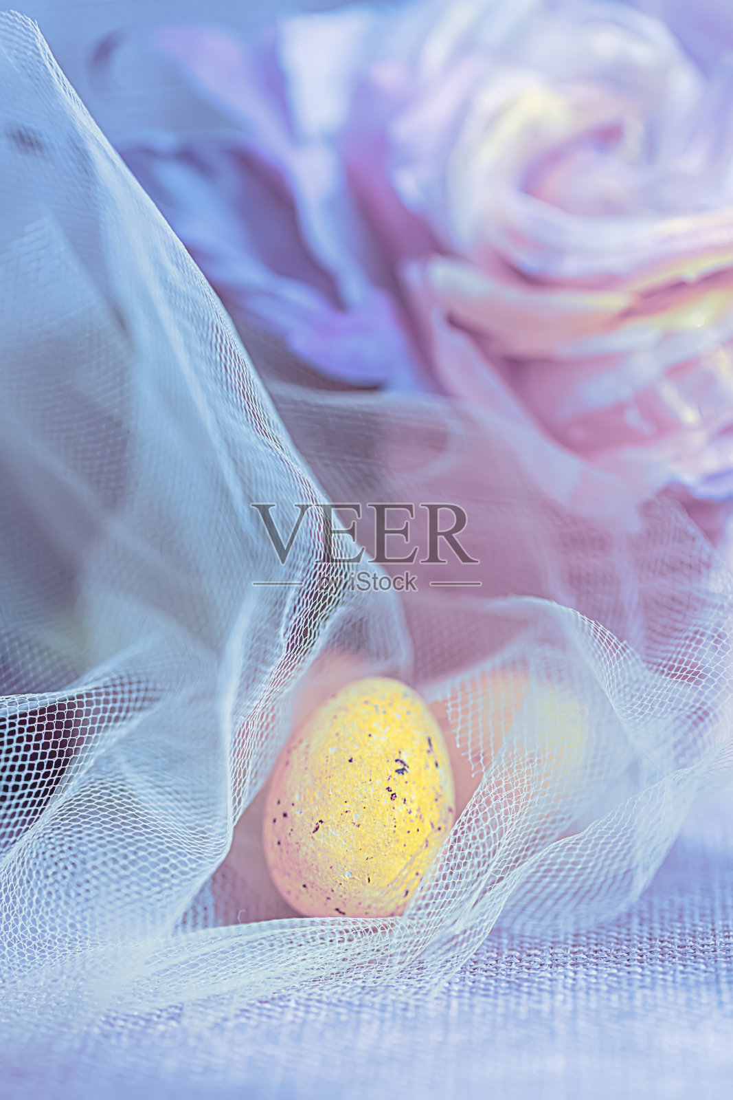复活节甜美的黄色鸡蛋在透明的蓝色布。模糊的背景与粉红色的花。特写镜头。浅景深照片摄影图片