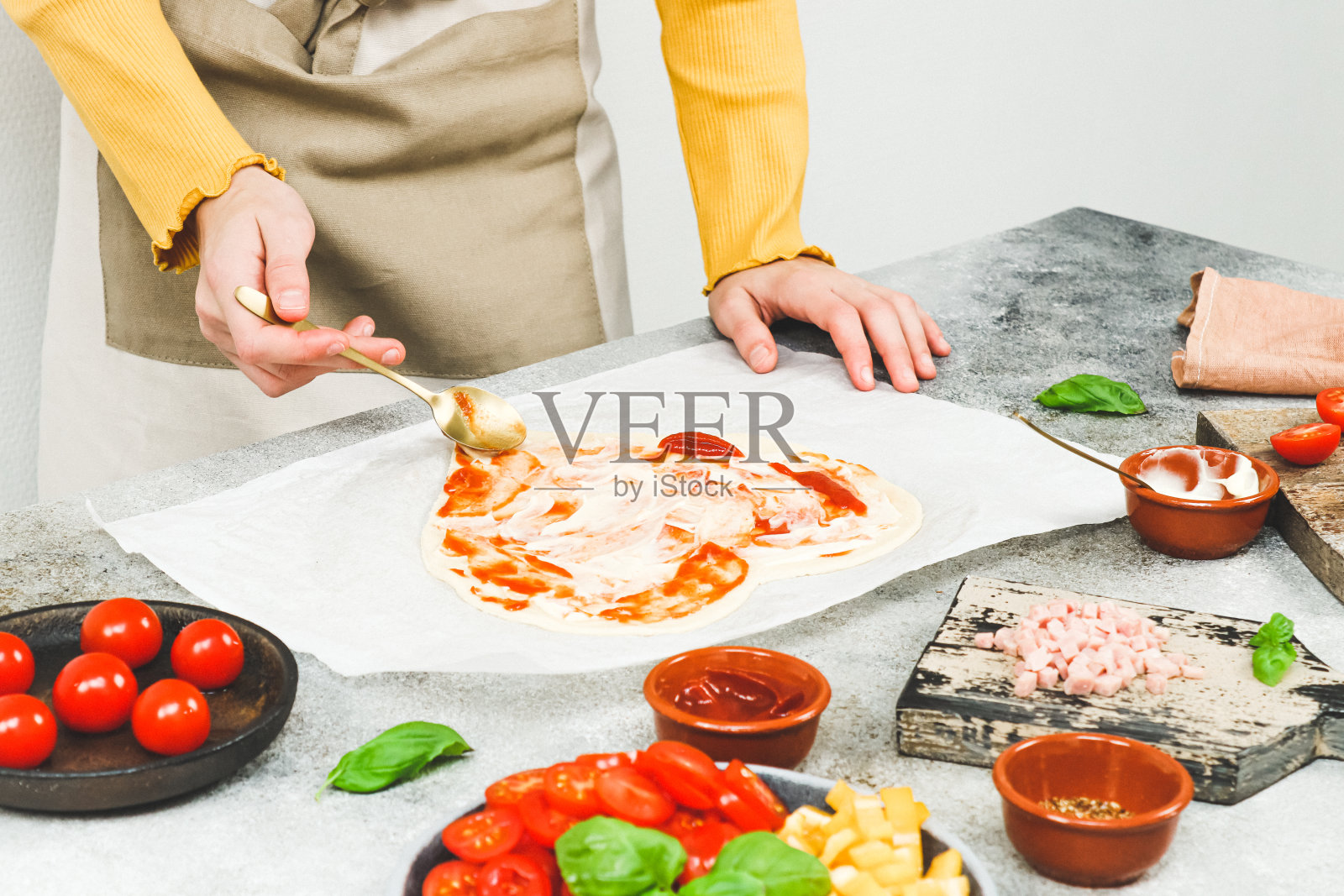 一个穿着围裙的白人少女的手把番茄酱涂在心形的披萨面团上照片摄影图片