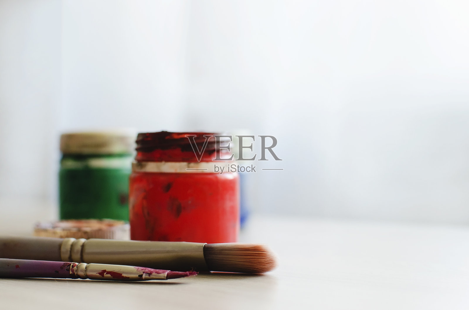 桌子上放着艺术家用过的脏兮兮的水粉颜料罐和画笔。中性的背景光。放置文本，copyspace。照片摄影图片