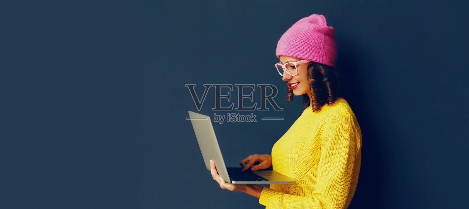 时尚现代年轻女性的肖像与笔记本电脑穿着色彩鲜艳的衣服在深蓝色的背景，横幅空白拷贝空间的广告文字照片摄影图片