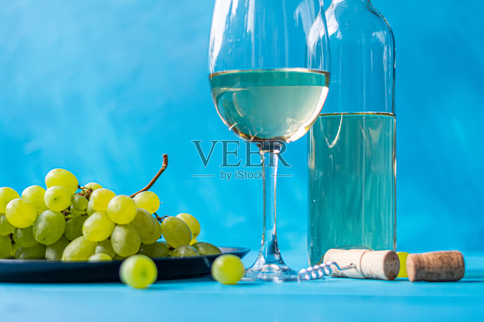 白葡萄酒在一个杯子的特写旁边的一个瓶子在自然上，在一个木制的年份蓝色的桌子上，绿色的葡萄枝。照片摄影图片