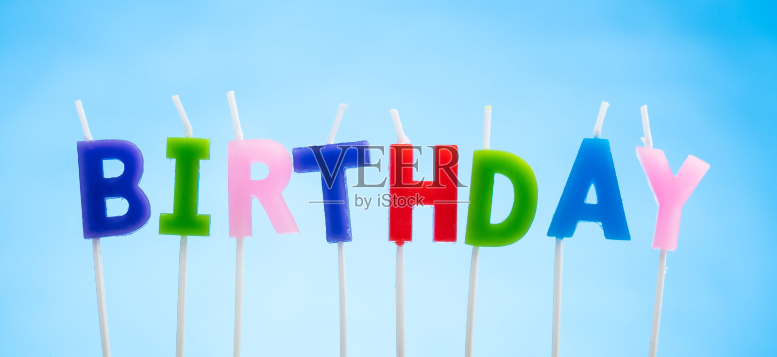 拼出生日字样的蓝色背景上的彩色蜡烛照片摄影图片