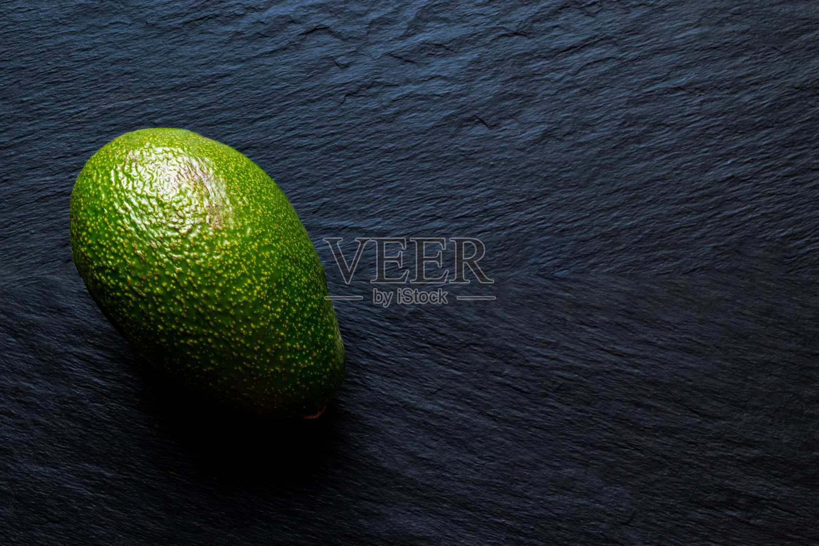 完整的绿色鳄梨果实在黑色的石头背景表面照片摄影图片