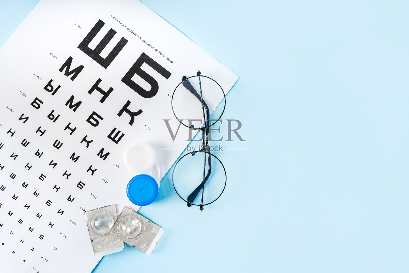 用俄语检查视力的桌子，浅蓝色背景的眼镜和镜头。眼科诊所或光学销售的概念照片摄影图片