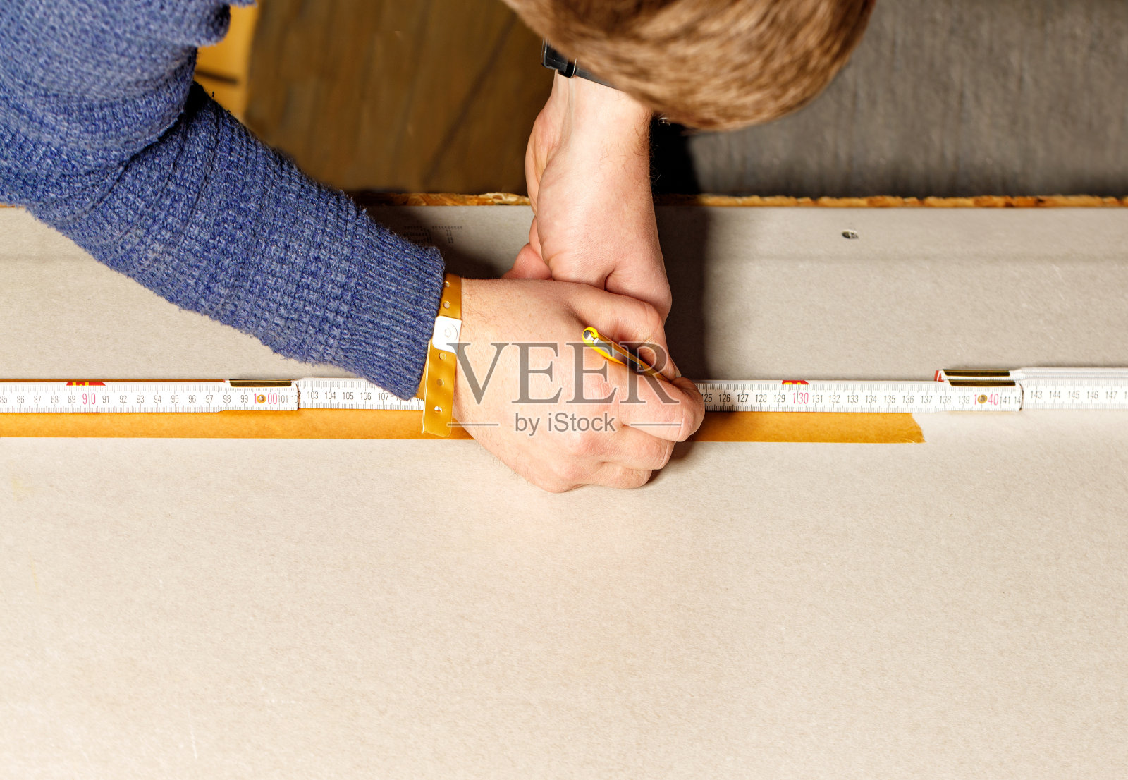 一名工人用铅笔和木折尺在一张干墙上画出记号。工人双手的特写。照片摄影图片