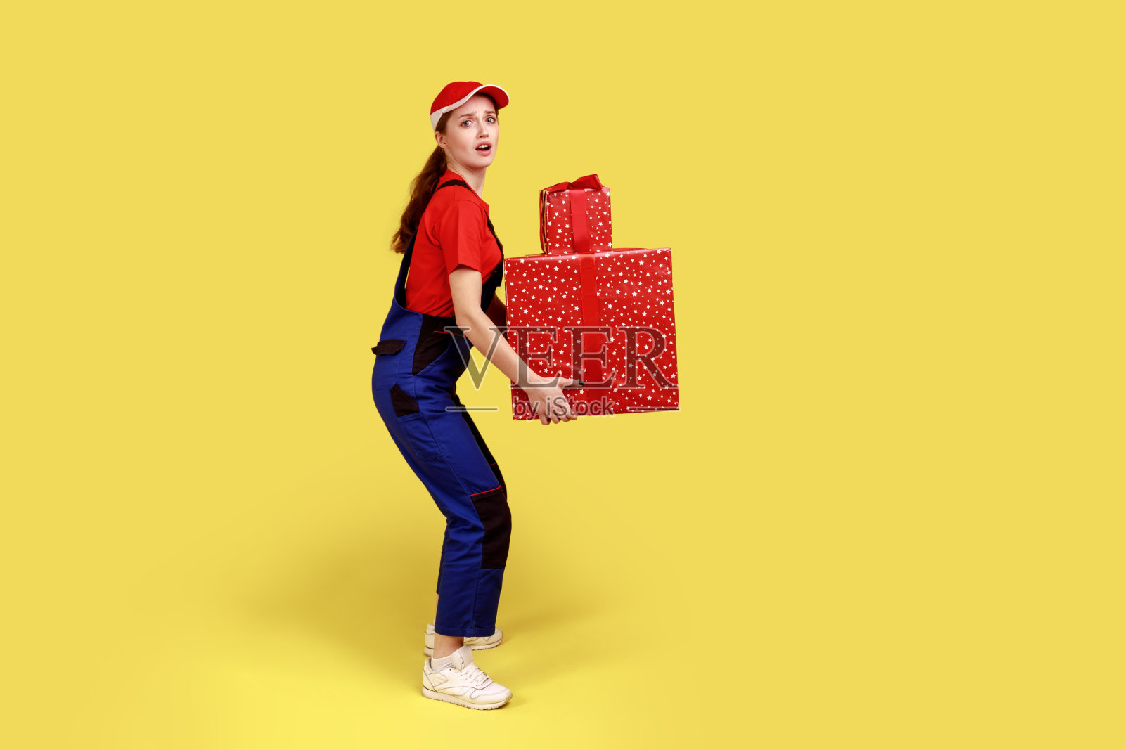 快递员拿着沉重的礼物盒子，看着摄像机，挨家挨户送货。照片摄影图片