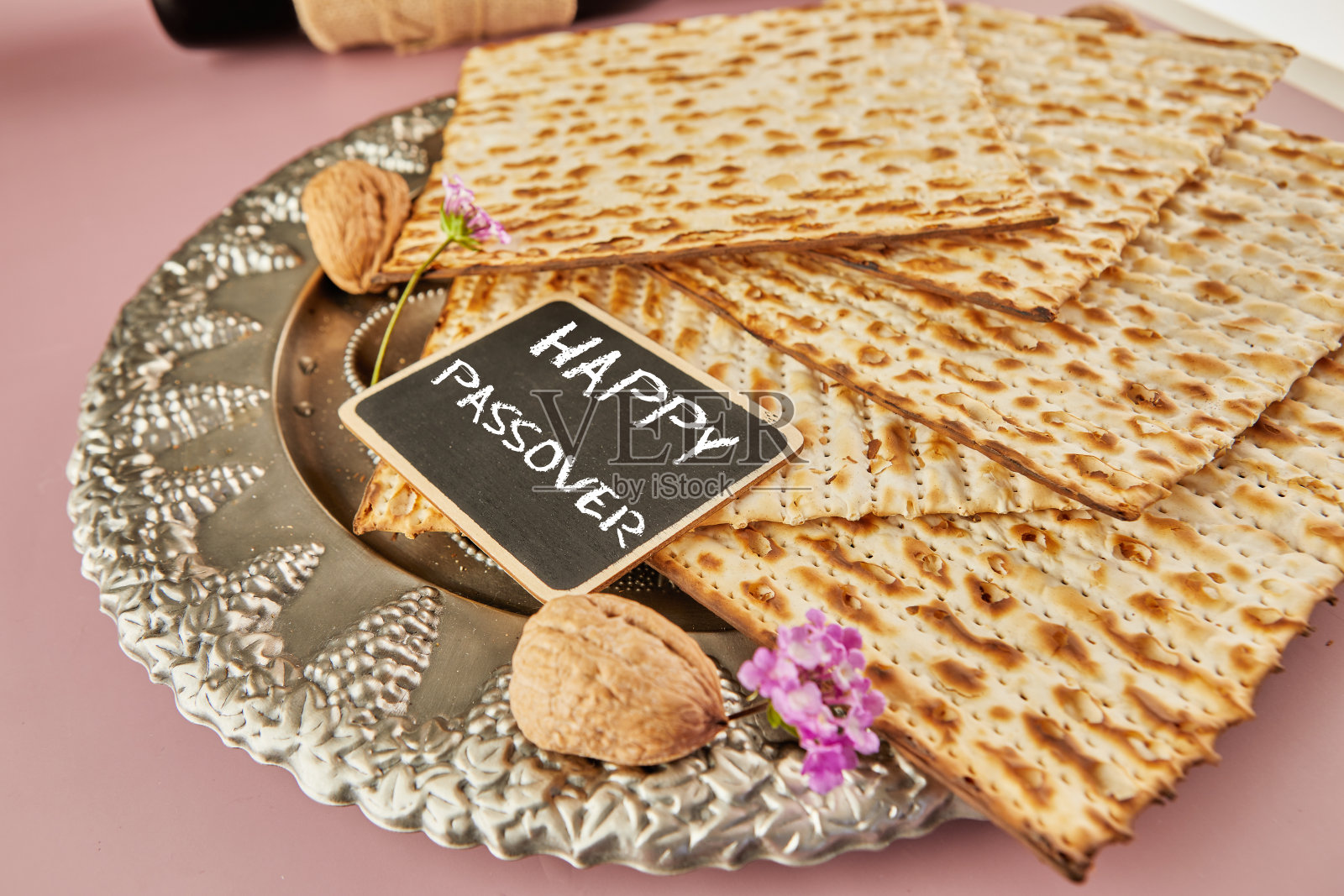 逾越节庆祝概念 - 犹太节日逾越节。传统逾越节盘子上的麦札，红酒瓶，紫色背景上的坚果和铭文“逾越节快乐”照片摄影图片