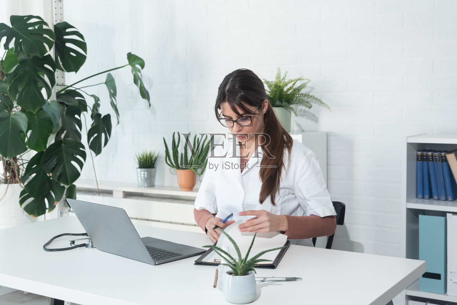 年轻快乐的女医生第一天上班或在她的新医院办公室工作。女性卫生保健工作者在诊所为在线病人工作。远程医疗的概念。用胶片颗粒照片摄影图片