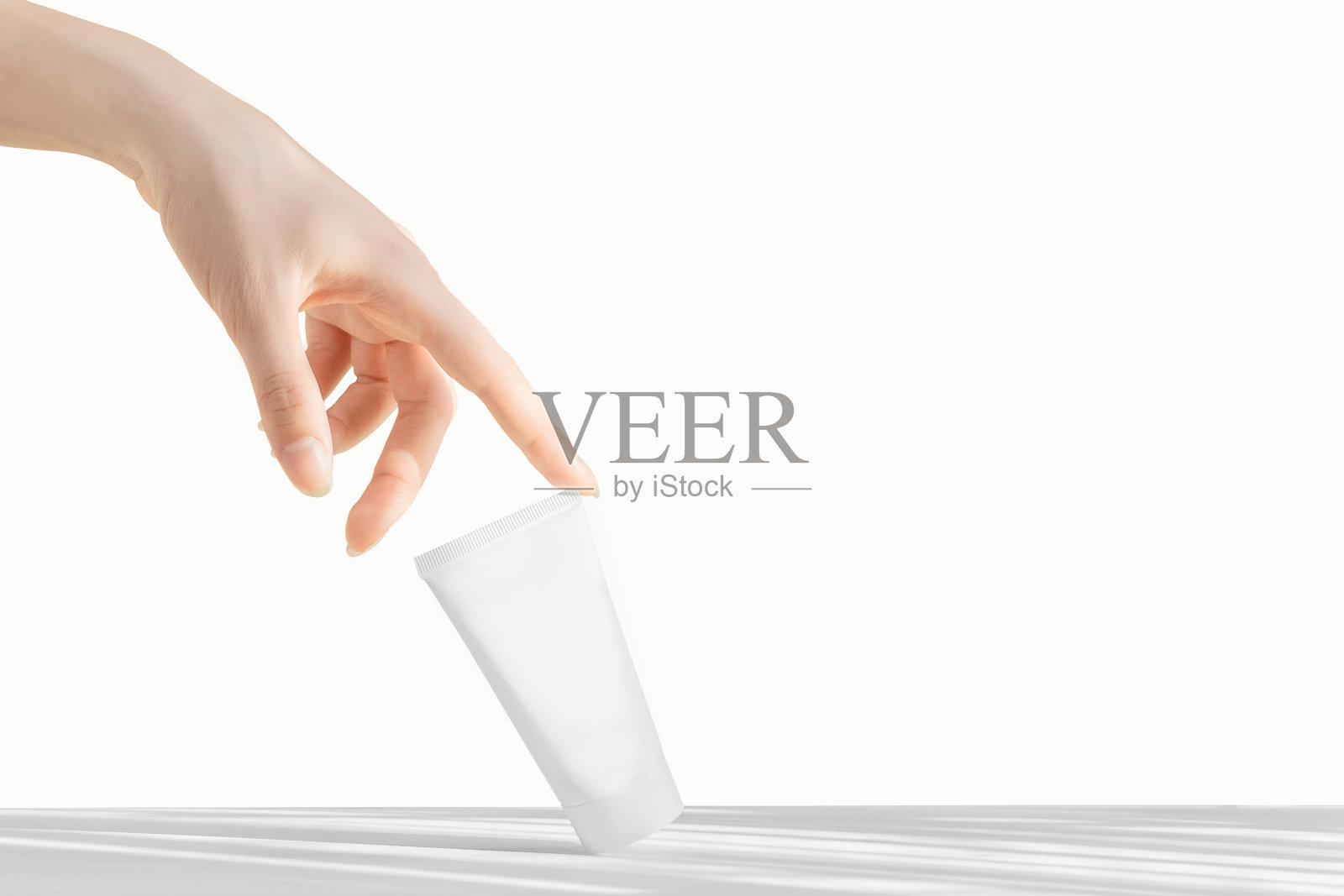 护肤理念。女人的手触摸白色的塑料奶油管。化妆品模型的特写镜头。白色的孤立的背景照片摄影图片