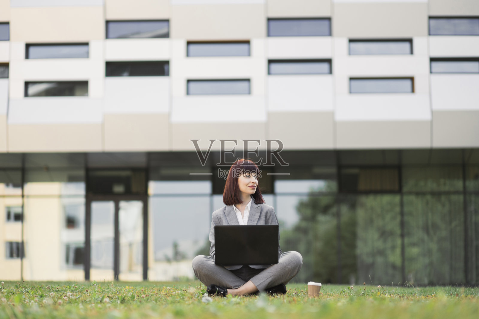 穿着西装的漂亮女人，坐在草地上用笔记本电脑，庆祝成功照片摄影图片