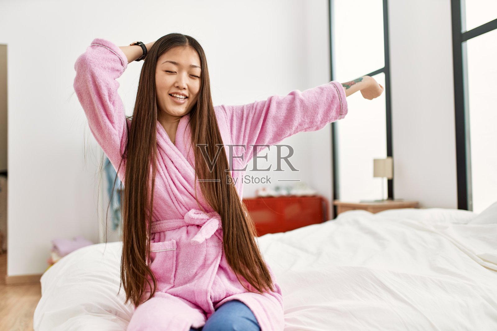 年轻的中国女孩坐在卧室的床上醒来。照片摄影图片