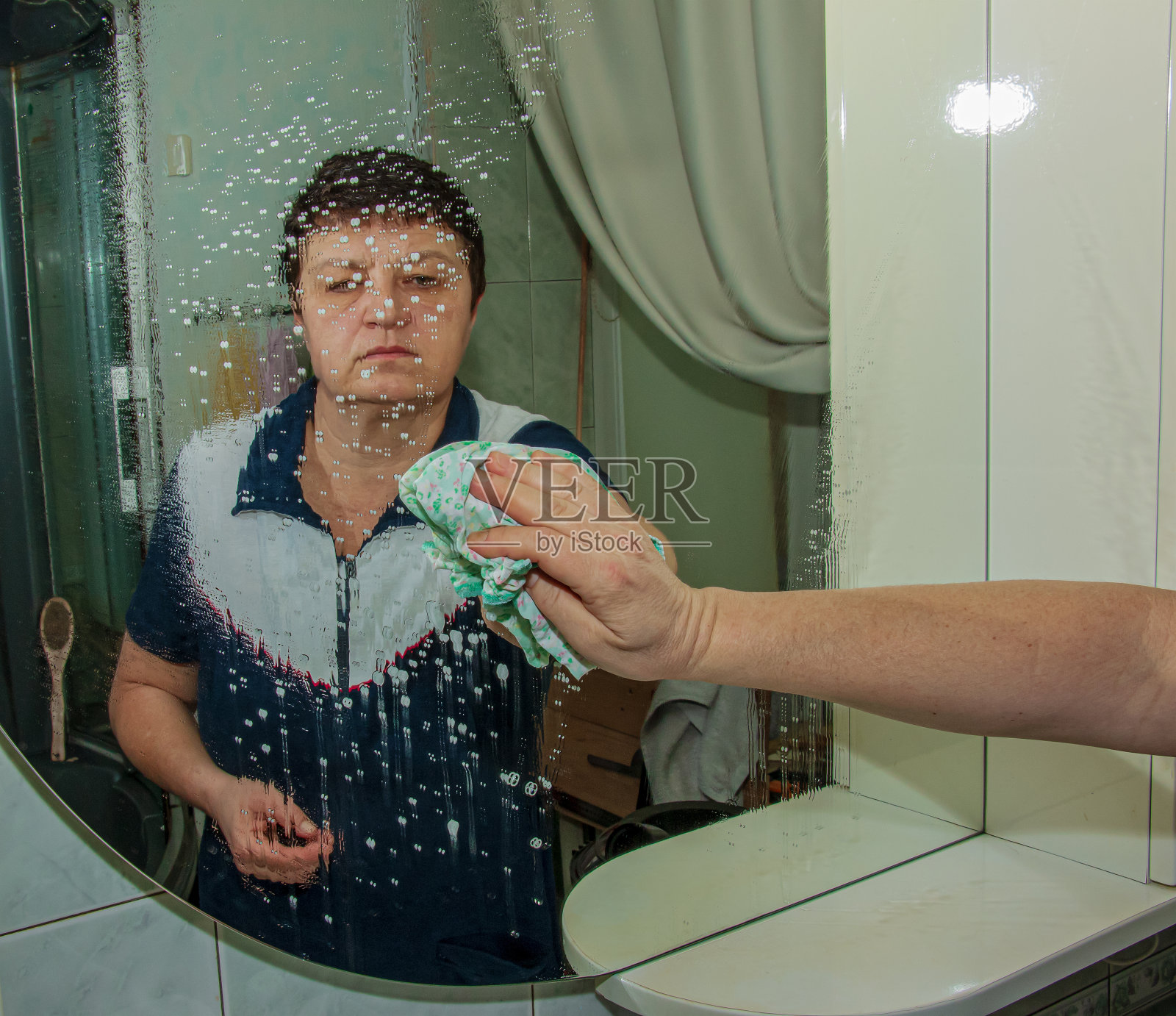 一名妇女在家里用餐巾擦镜子上的污垢和水匾照片摄影图片