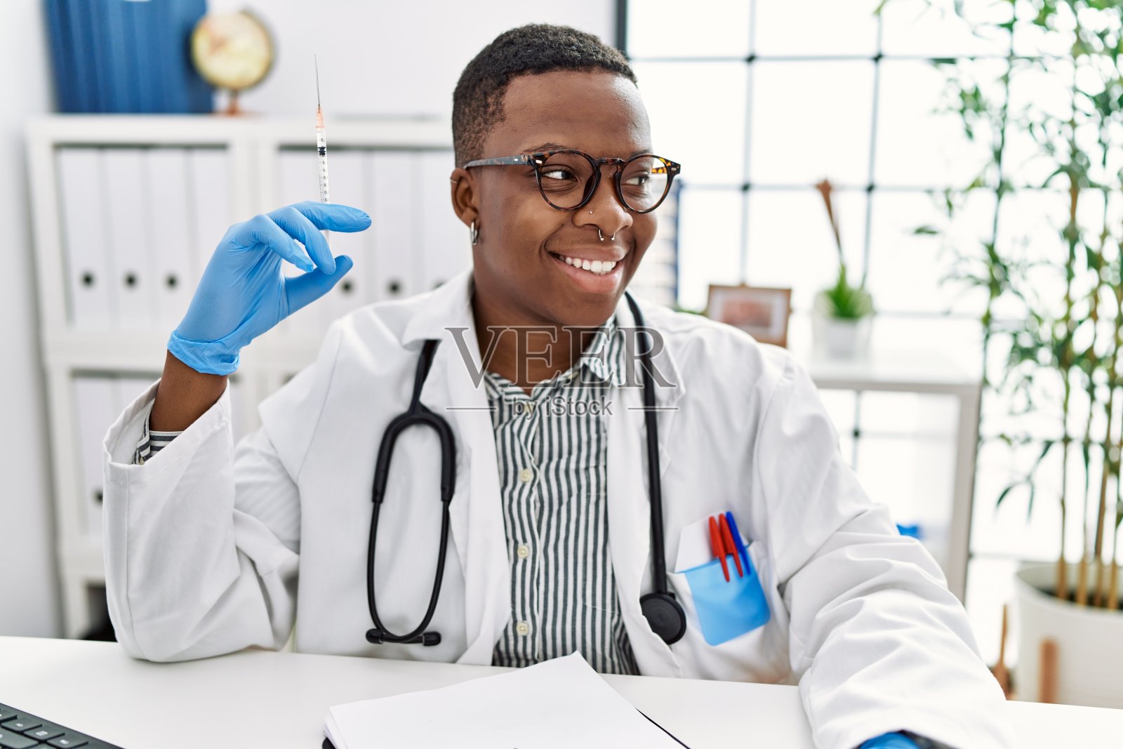 年轻的非洲医生拿着注射器在医院里望向一边，面带微笑，表情自然。自信的笑。照片摄影图片