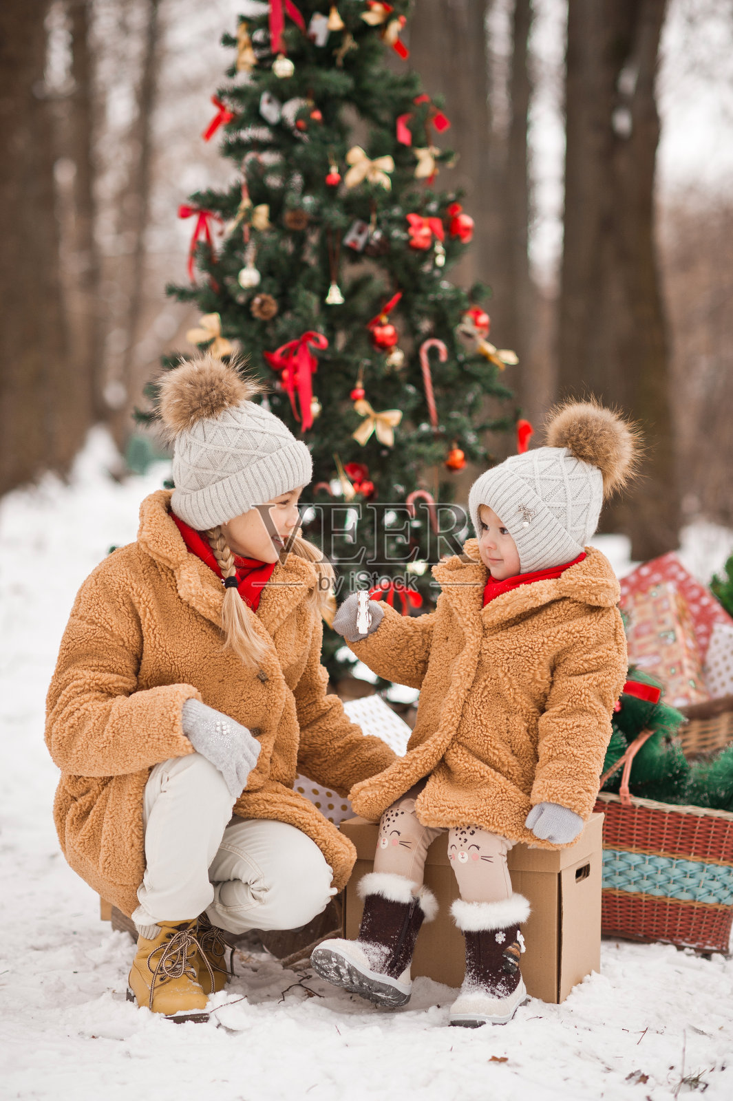 在冬天的雪中，孩子们在装饰好的圣诞树旁玩礼物照片摄影图片