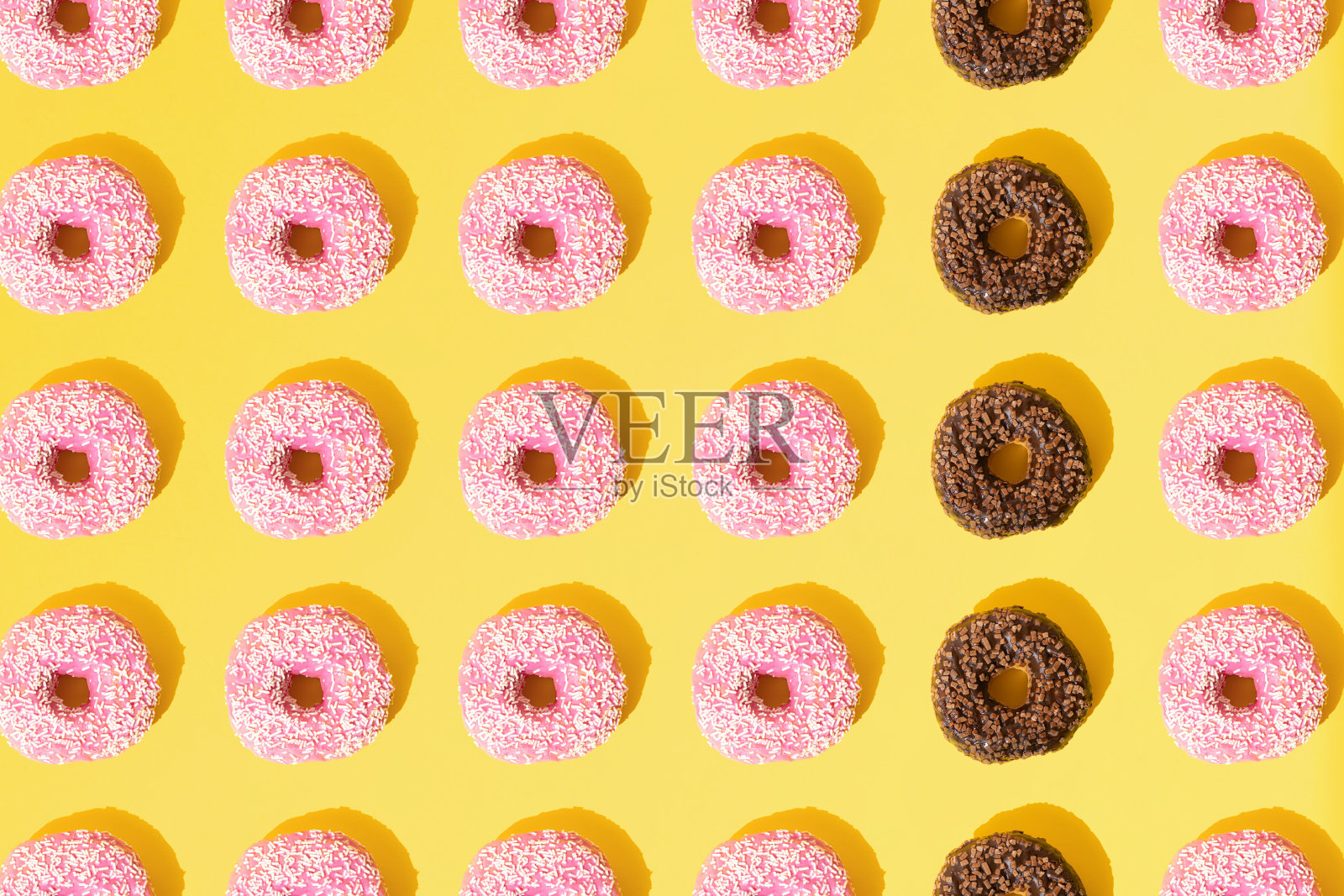 粉红色和巧克力色的环形甜甜圈。白色和棕色的小碎屑在黄色的粉彩背景上。模式。平的。照片摄影图片