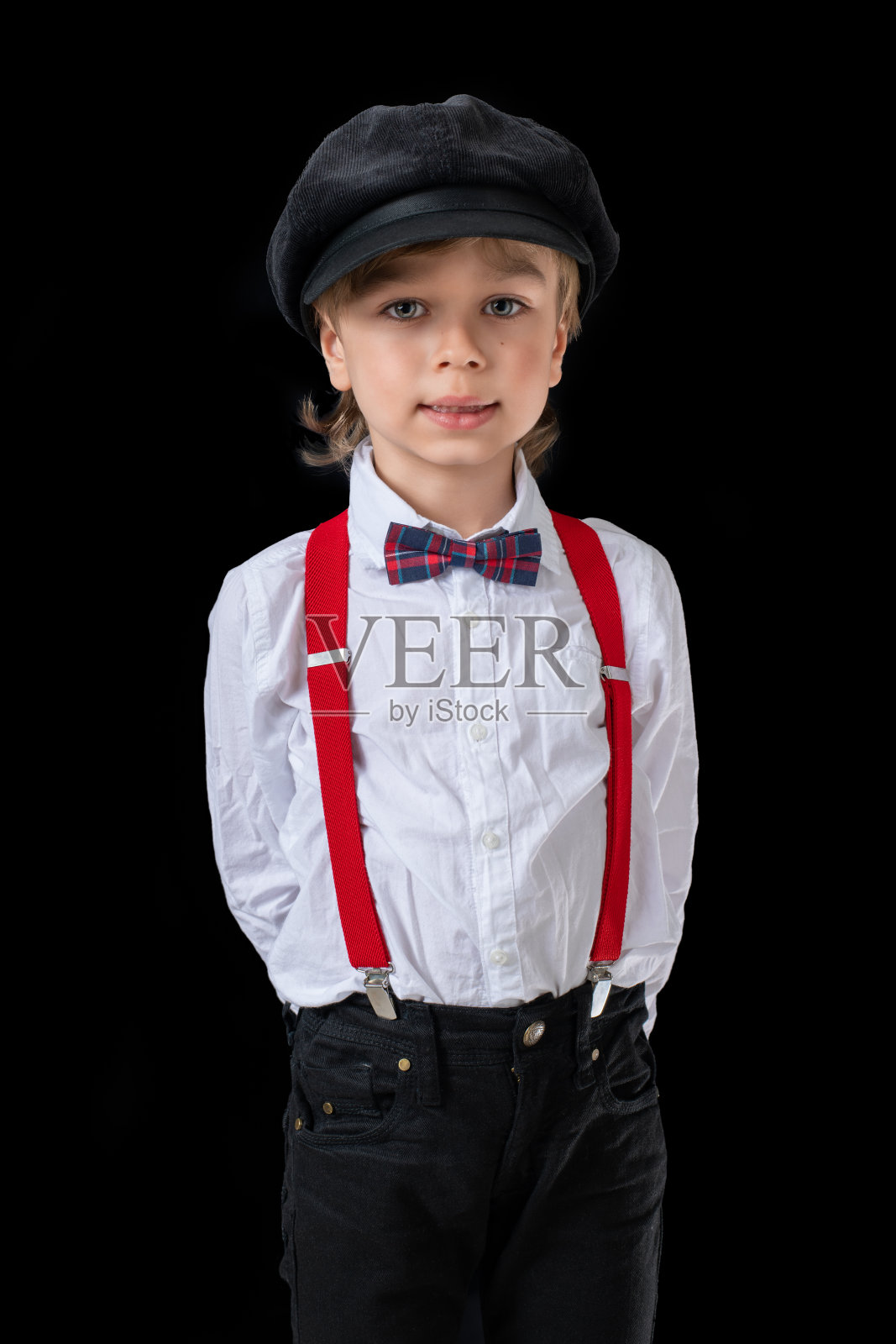 可爱的学龄前小男孩，穿着漂亮，在黑色的背景上戴着帽子摆姿势。照片摄影图片