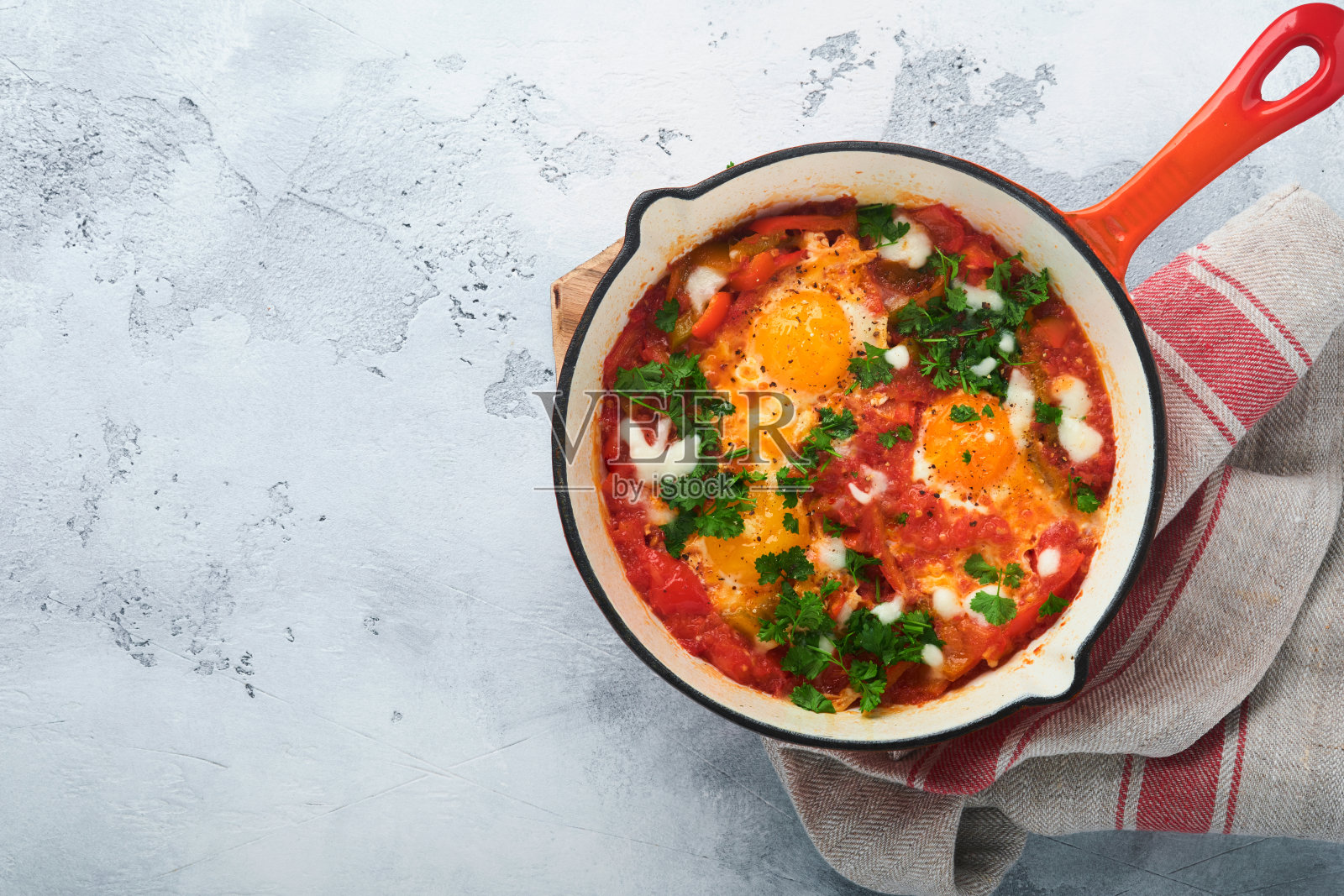 Shakshuka。在浅灰色的石板、石头或混凝土背景上，用铁锅煎鸡蛋和蔬菜。以色列的传统菜肴。晚早餐概念。顶视图,横幅照片摄影图片